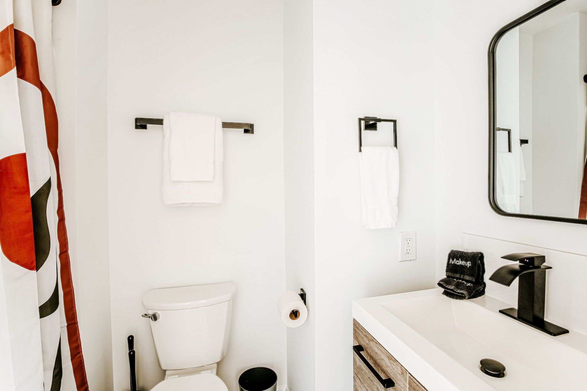 A bathroom with a toilet, a towel rack, a sink with a mirror, and a black towel labeled 'Makeup'.