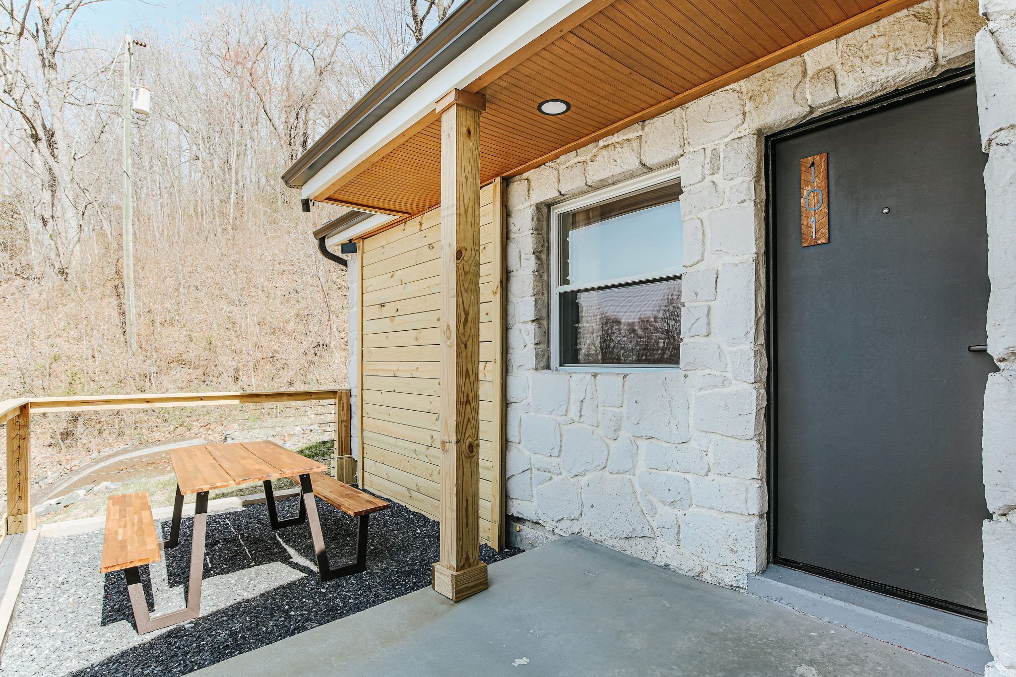 Una terraza de madera con una mesa de picnic, un muro de piedra y una puerta oscura.
