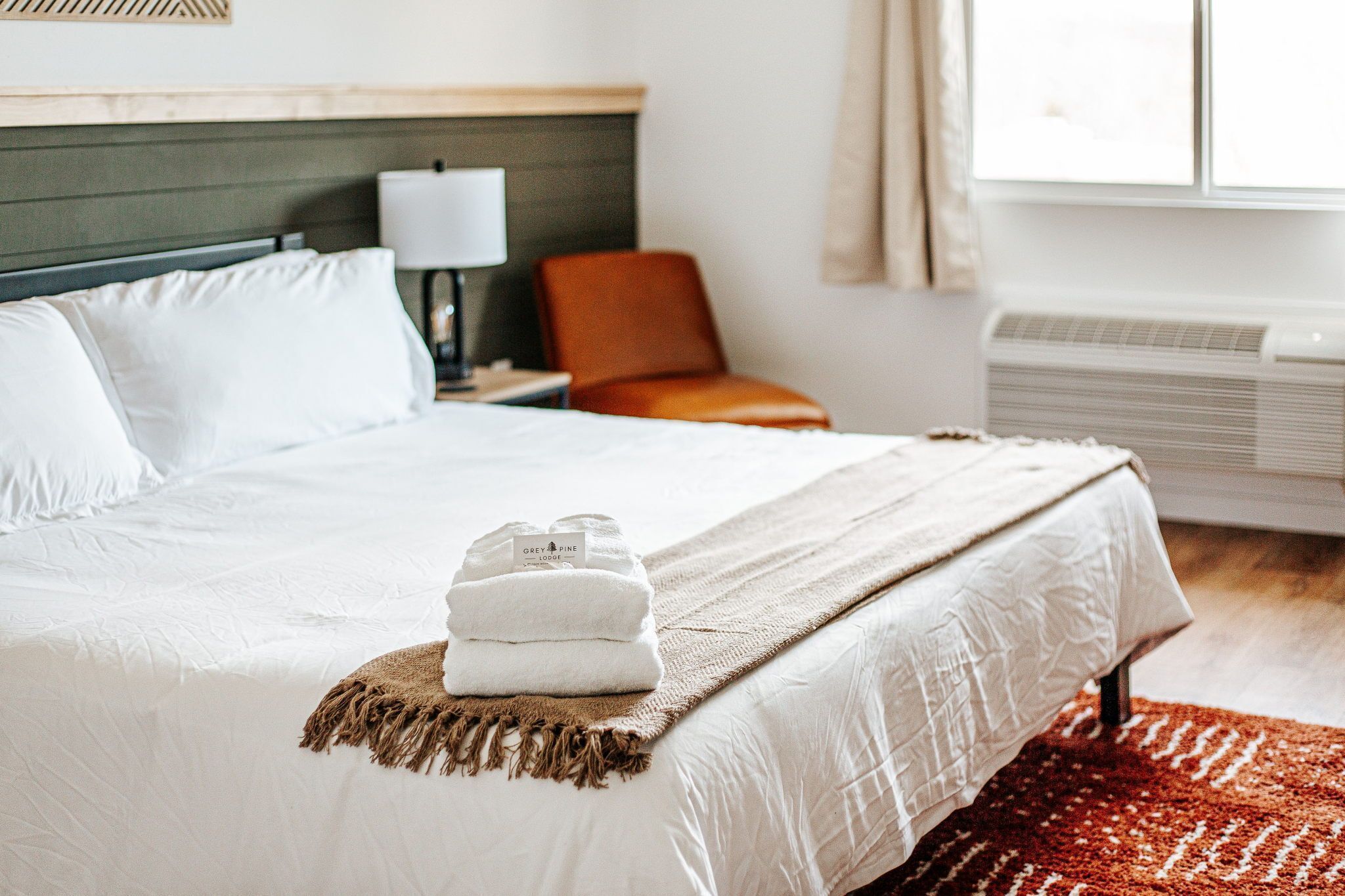 A hotel room with a bed, a nightstand, a lamp, a chair, and a window.