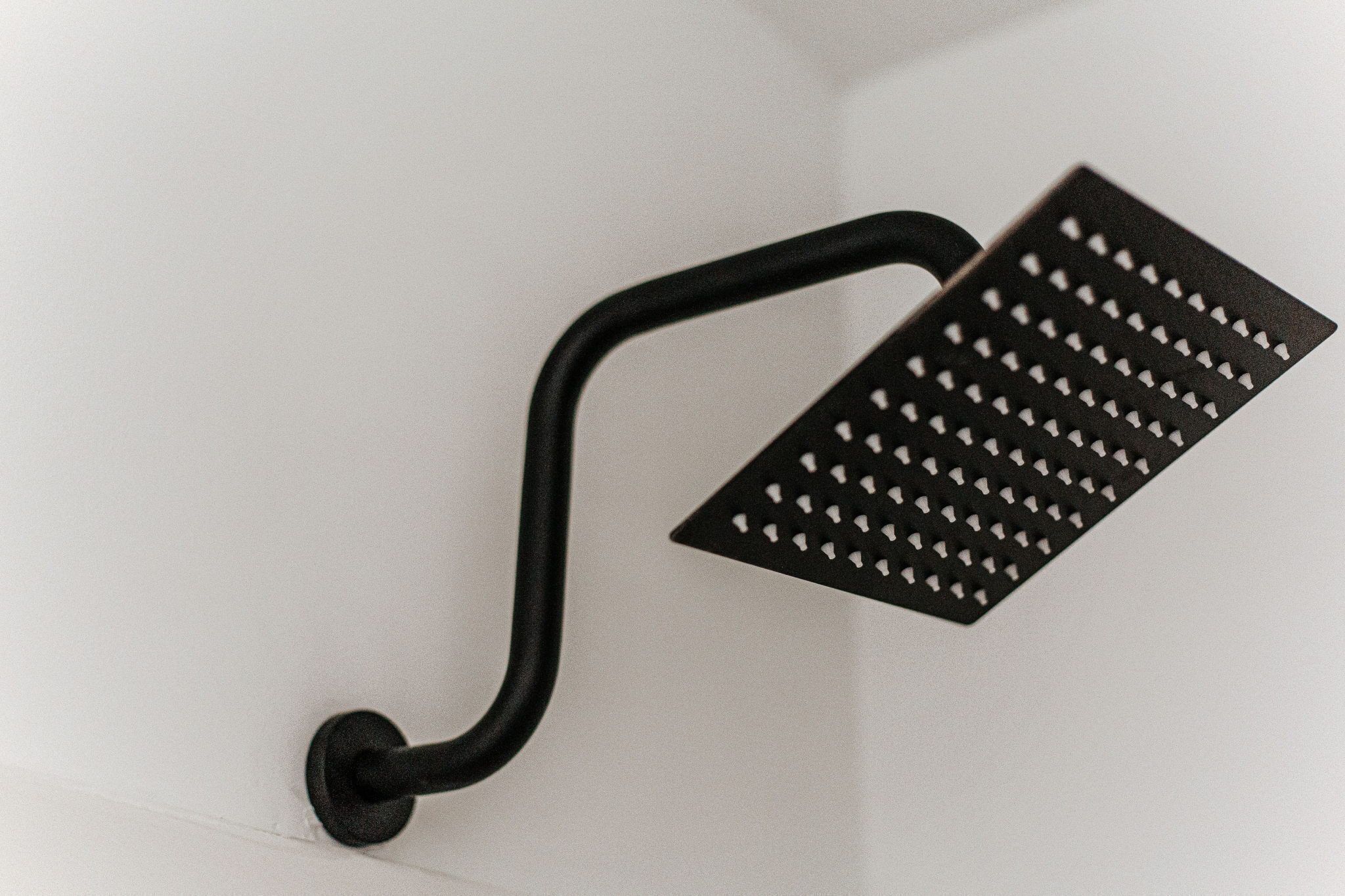 Un objeto de metal negro con asa curva y superficie perforada, montado sobre una pared blanca.