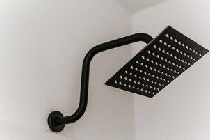 Un objeto de metal negro con asa curva y superficie perforada, montado sobre una pared blanca.