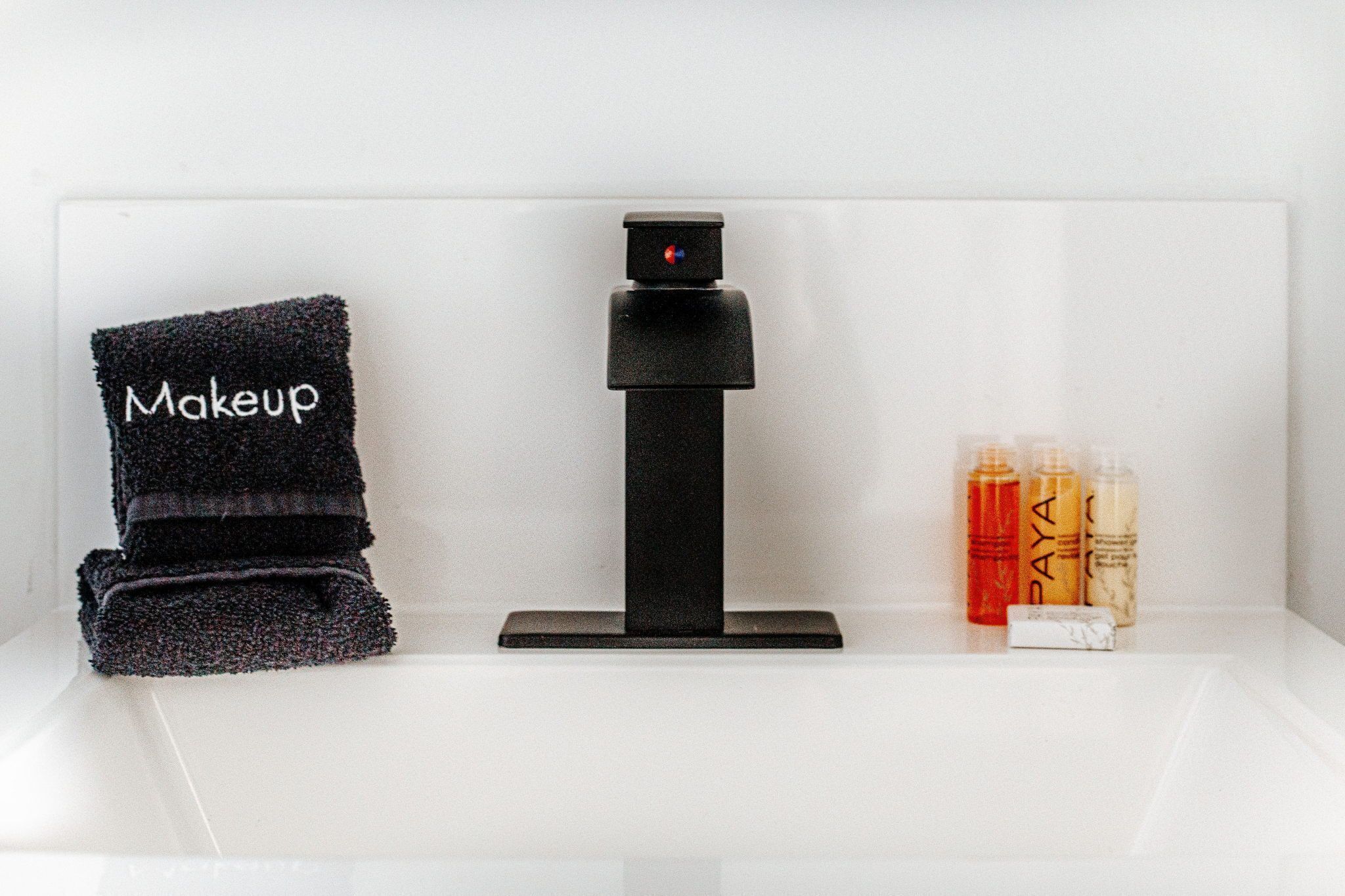 A bathroom with a towel rack holding a towel labeled 'Makeup,' a black handheld mirror, and two bottles of lotion.