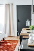 Una habitación moderna con cama, escritorio, silla, planta en maceta y una puerta.