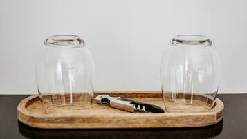 Un plateau en bois sur lequel reposent deux verres à vin vides et un tire-bouchon, le tout posé sur une surface sombre.