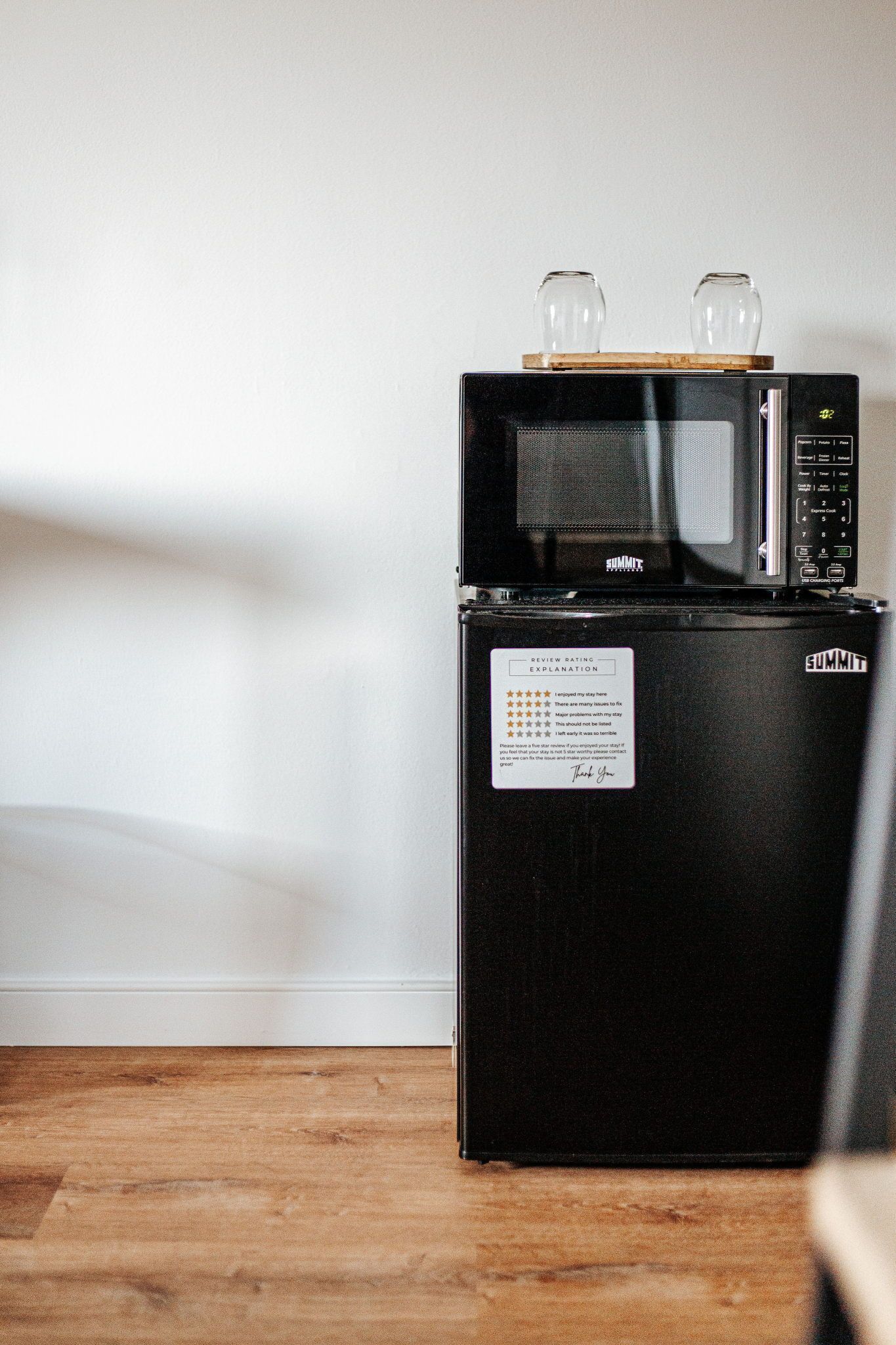 Un refrigerador negro con un microondas encima, un estante de madera con dos vasos y una etiqueta con una reseña.