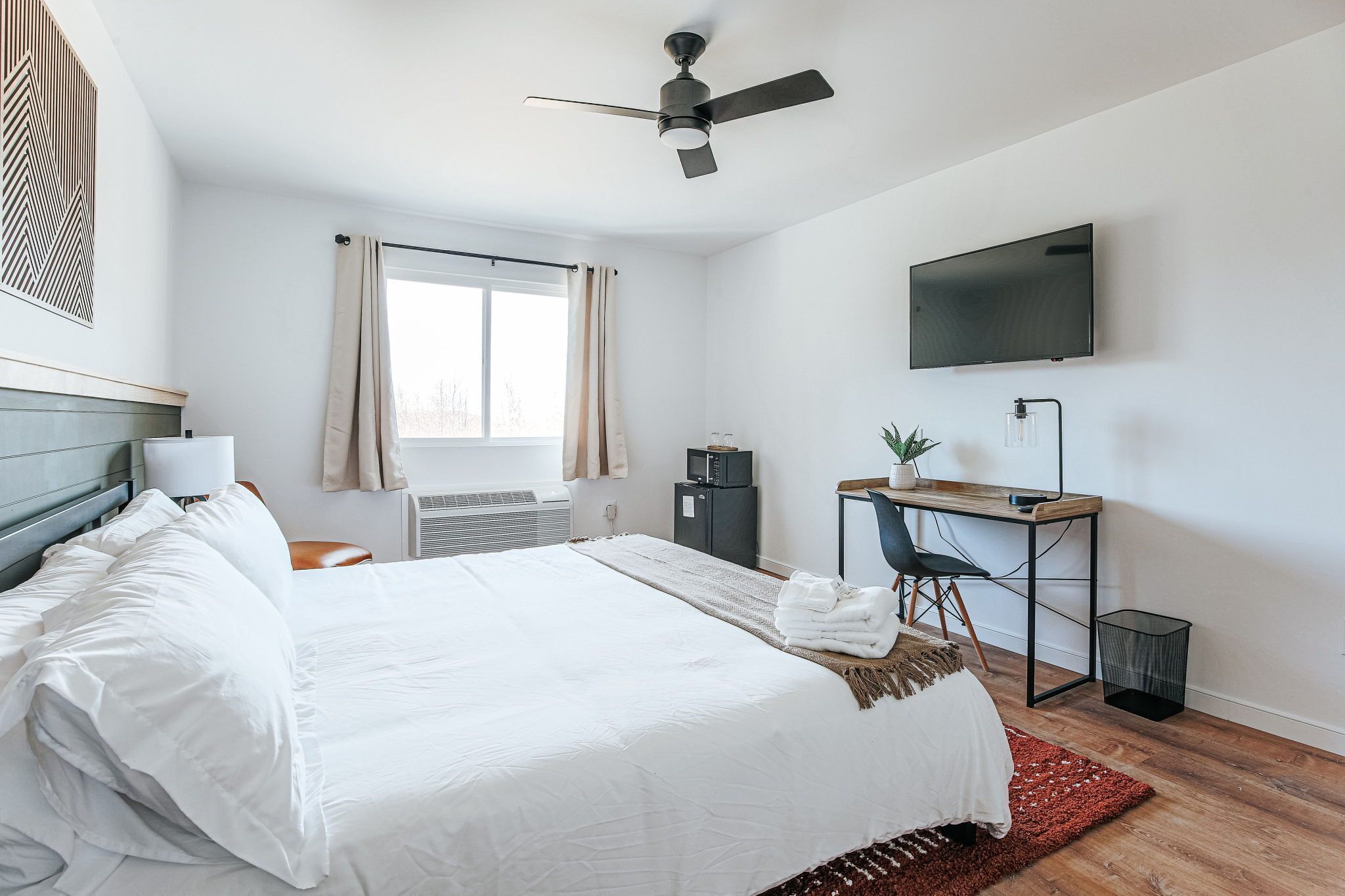 Habitación de hotel con cama, escritorio, silla, televisor y ventana.