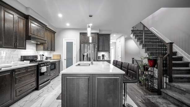 A modern kitchen with dark wood cabinets, a large island, and a staircase leading to a second floor.