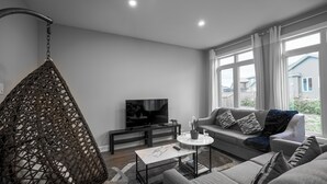 A modern living room with a hanging chair, a sofa, a coffee table, and a TV.
