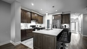 A modern kitchen with dark wood cabinets, a marble countertop, stainless steel appliances, and a bar seating area.