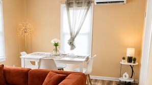 Une pièce comprenant un canapé, une table à manger avec des chaises, une petite table avec une lampe et un appareil de climatisation fixé au mur.