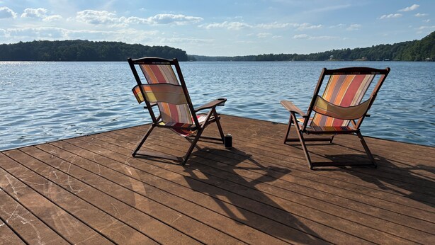 Deux chaises longues rayées sont posées sur une terrasse en bois, d’où l’on a vue sur un lac paisible bordé d’une forêt.