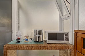 A kitchenette with a coffee maker, a microwave, and a small coffee grinder on a wicker table.