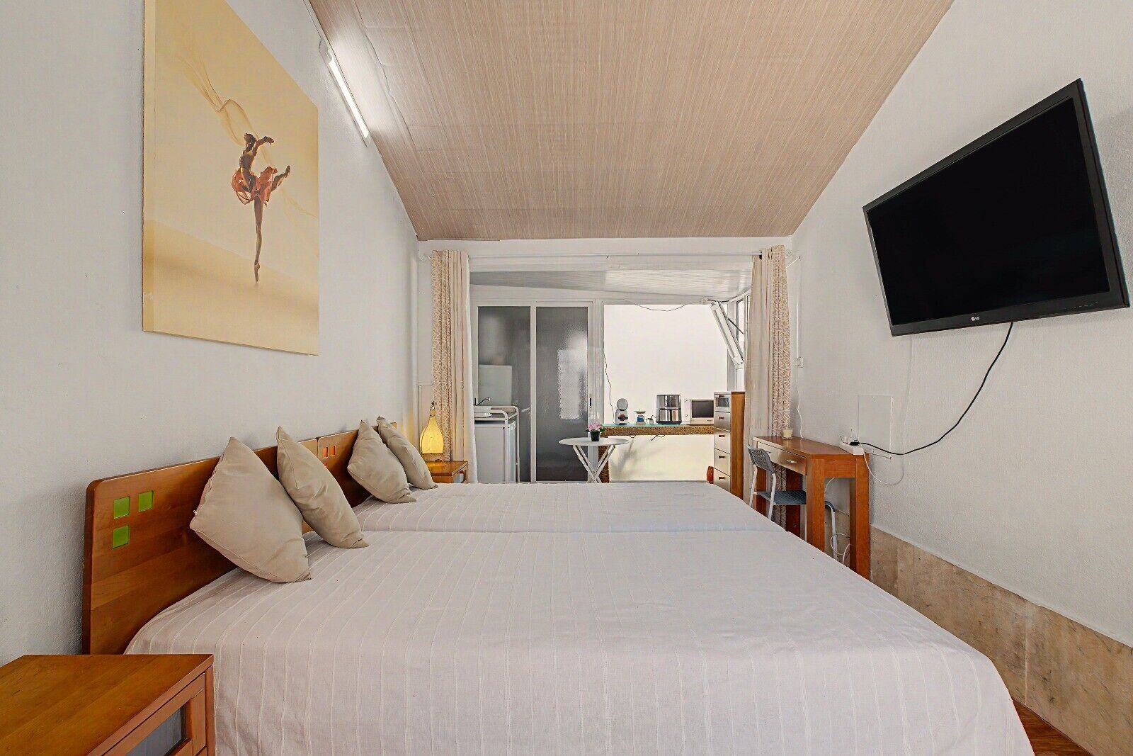 A hotel room with a bed, a television mounted on the wall, and a view of the balcony.