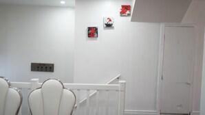 Een hotelkamer met een witte muur, een deur en een trap. Er hangen drie kunstwerken aan de muur.