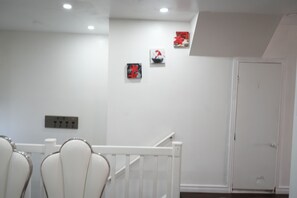 A hotel room with a white wall, a door, and a staircase. There are three artworks on the wall. - Bright 3BR Home | Explore Niagara & Beyond (Welland)