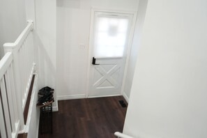 A hallway with a white door, a small window, and a shoe rack. - Bright 3BR Home | Explore Niagara & Beyond (Welland)