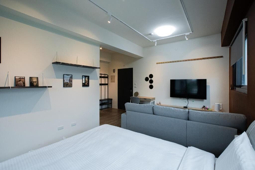 Habitació d'hotel moderna amb un llit, un sofà gris, una televisió i obra d'art a les parets.