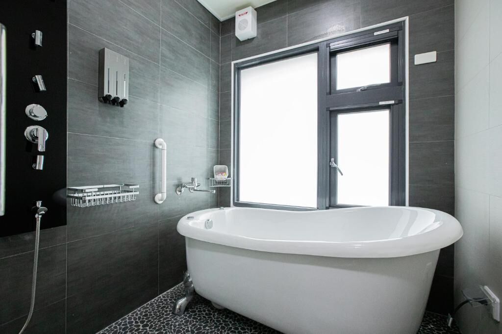 A modern bathroom with a freestanding bathtub, a shower, and a window.