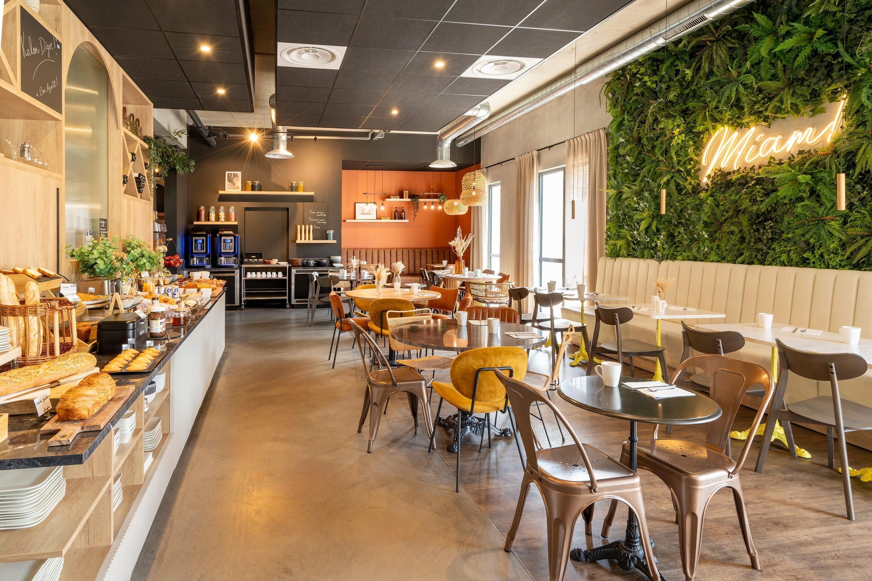 A cafe interior with a breakfast bar, seating area, and a green wall with a neon sign.