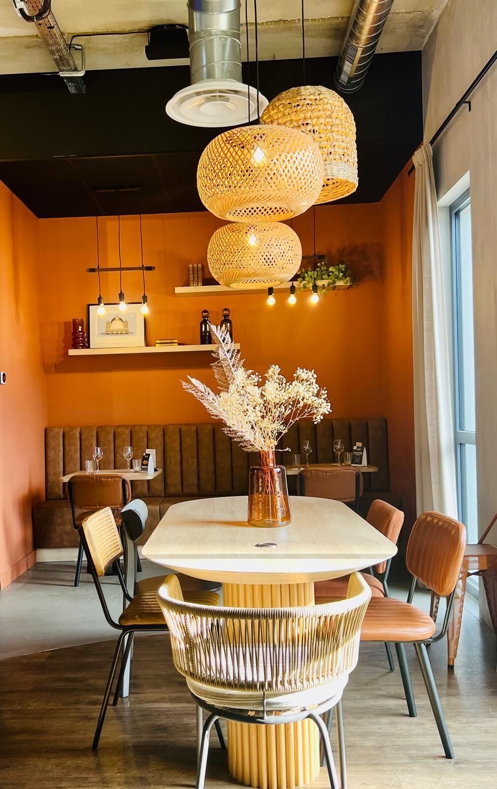 A dining area with a round table, wicker chairs, and a vase with dried flowers.