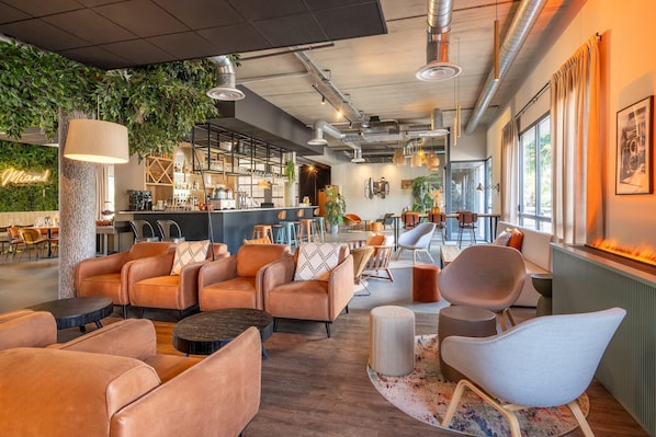 A modern lounge area with leather sofas, a bar with shelves of bottles, and a large window with curtains. - Best Western Plus Hotel De Robien (Saint-Brieuc)