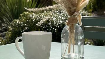 A white mug, a clear glass bottle with pampas grass, and a spoon on a white napkin on a table.