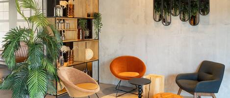 Una sala moderna con una estantería de madera, dos sillones, un otoman redondo y un espejo grande en la pared.