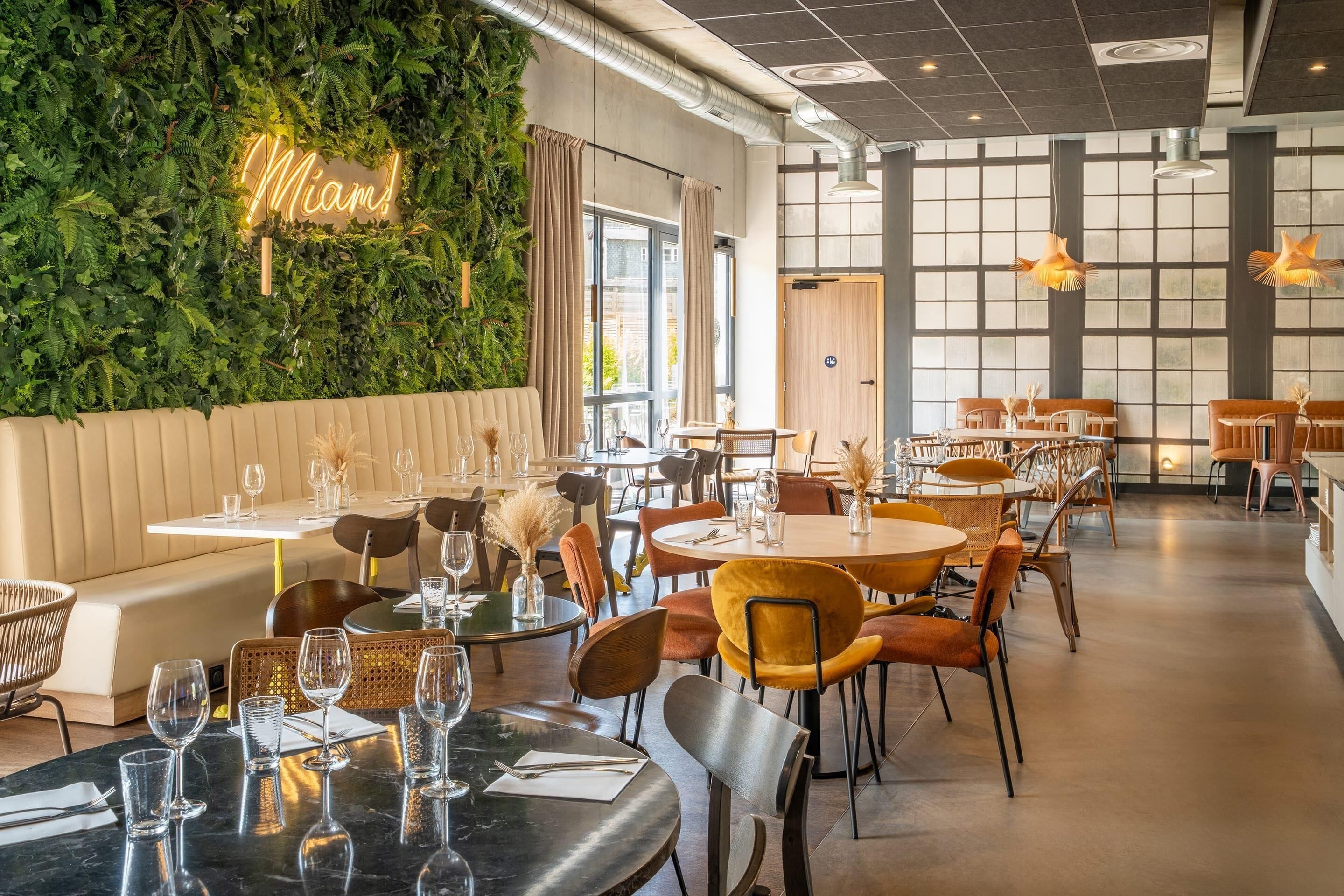 Interior de un restaurante con una pared verde, varias mesas y sillas.