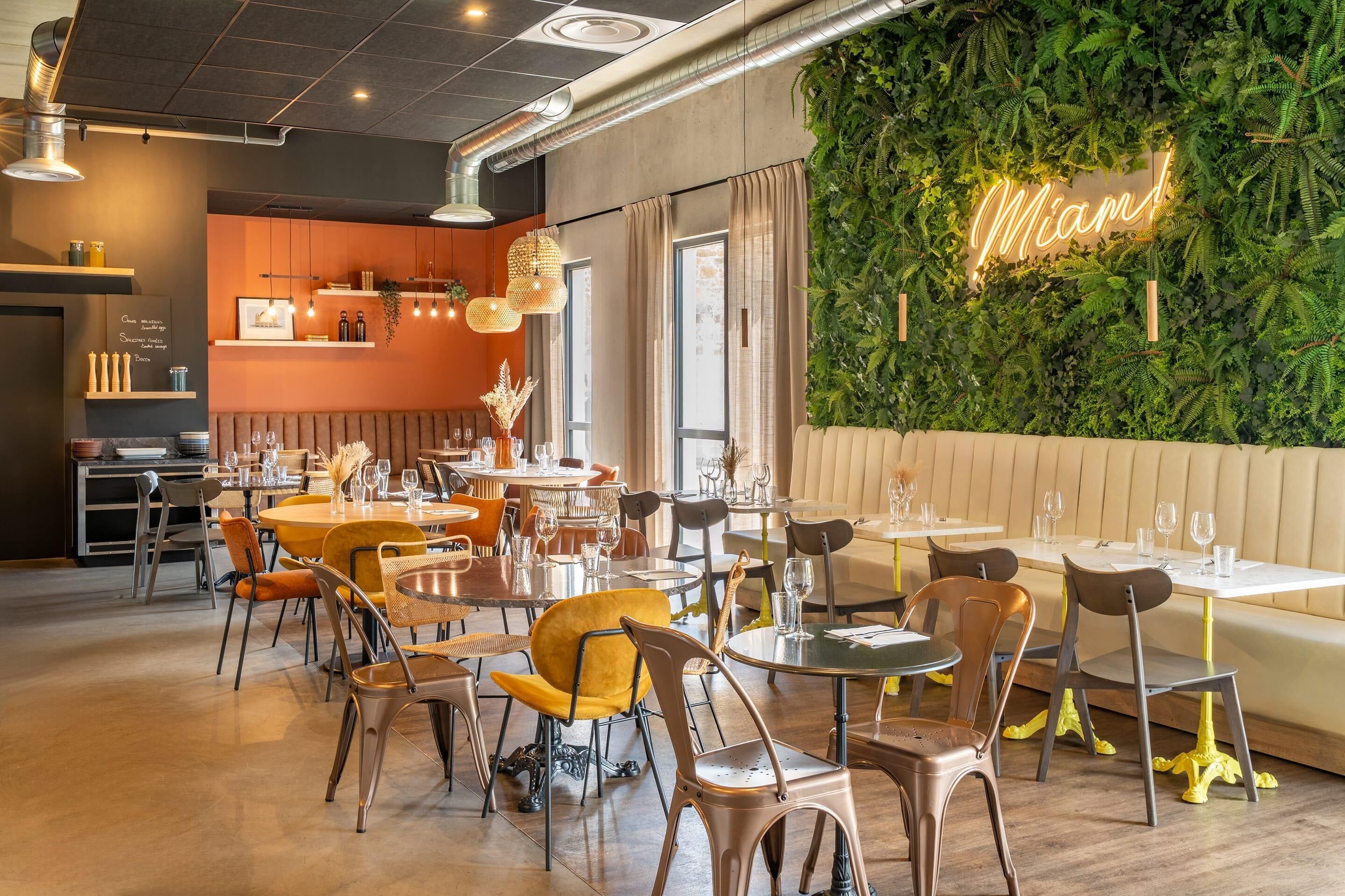 Ein Restaurantinneres mit grüner Wand, einer Neonreklame und unterschiedlichen Sitzmöglichkeiten.