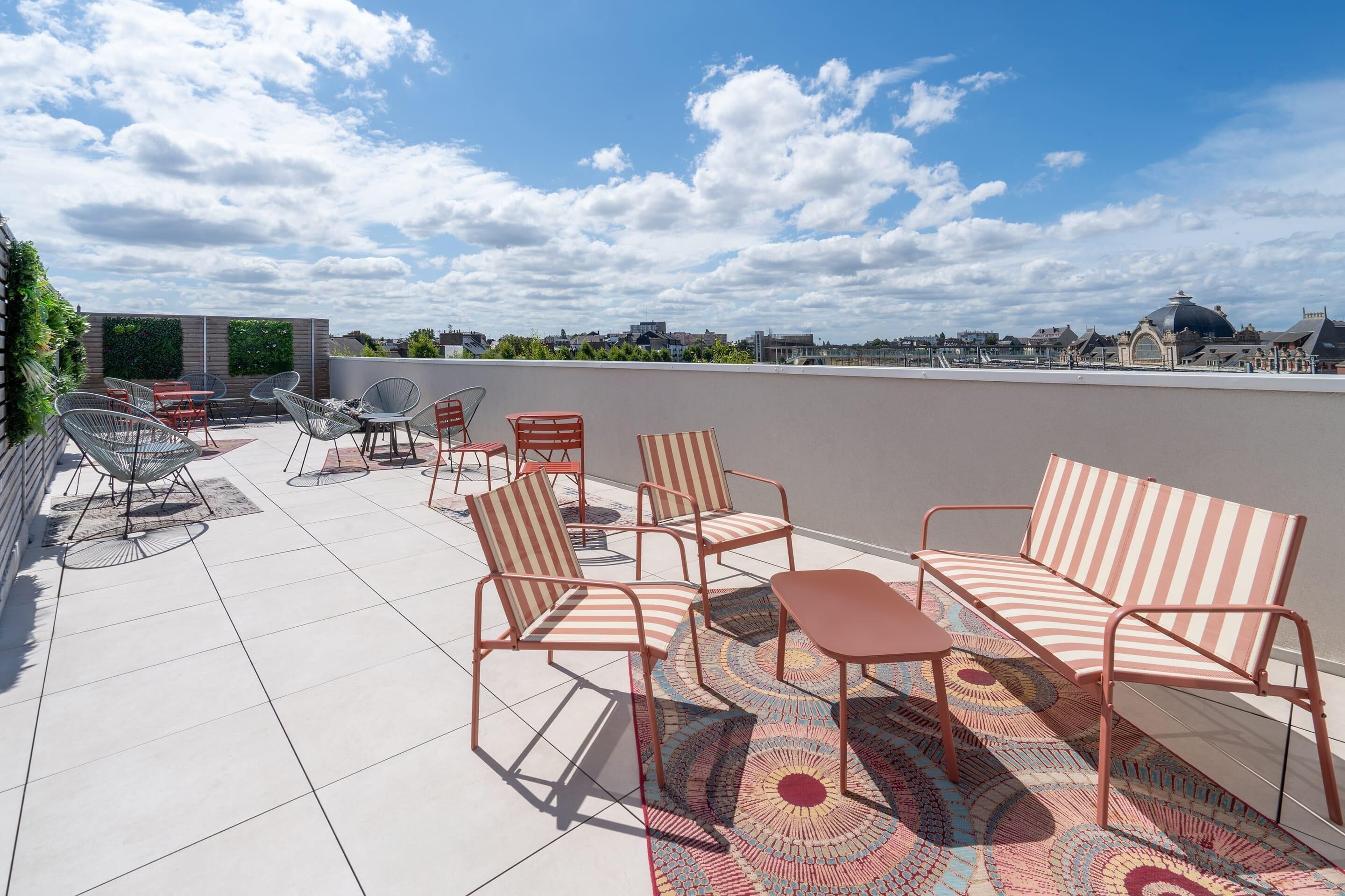 Una terraza en la azotea con mobiliario exterior, incluyendo sillas y una mesa, y vistas a la ciudad de fondo.