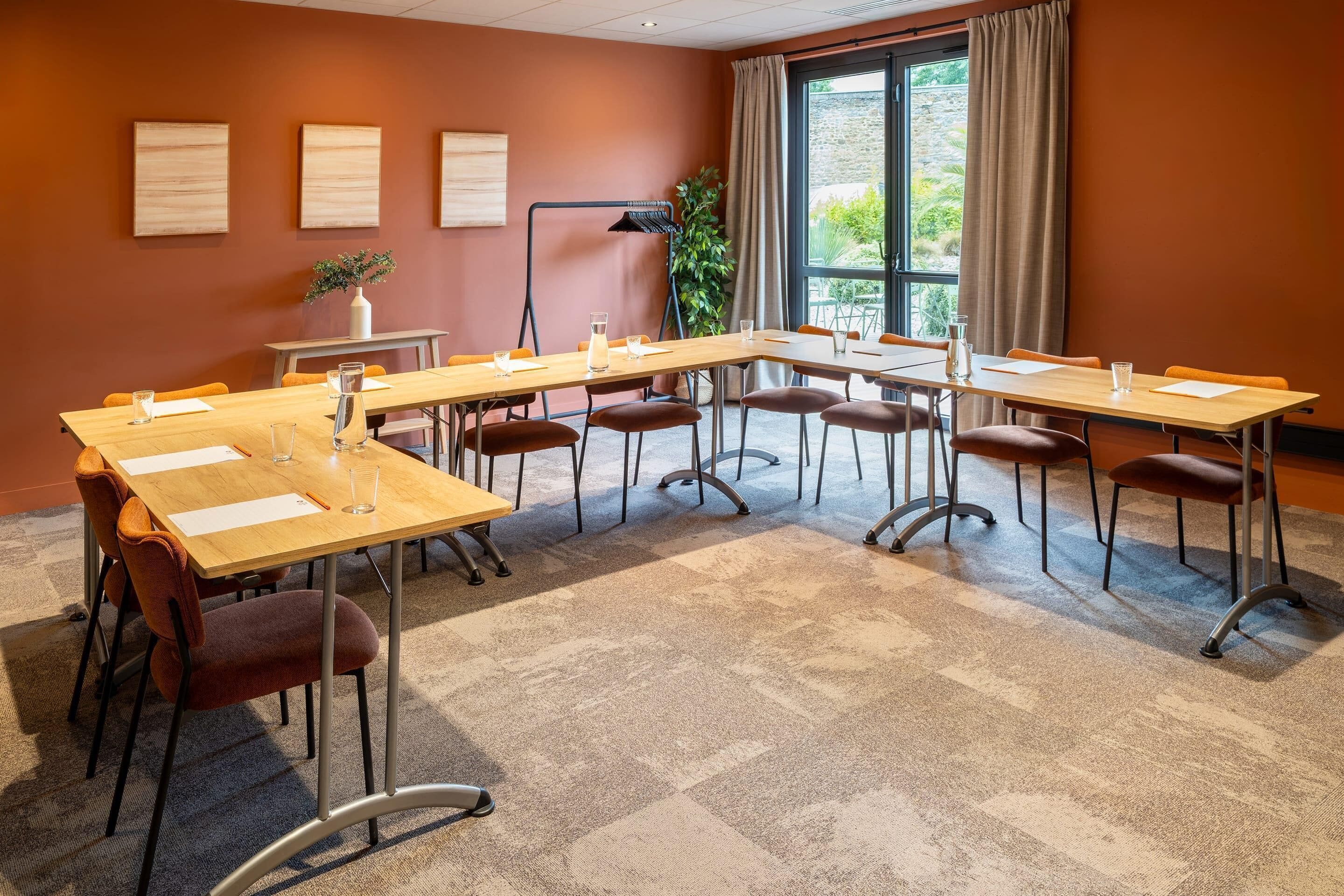 A conference room with multiple tables and chairs, a large window with curtains, and a plant on the windowsill.