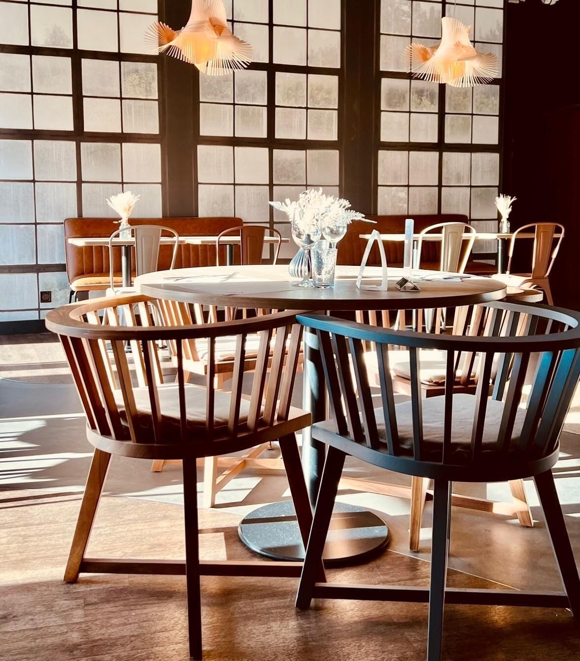 Une table de salle à manger ronde, entourée de chaises, un vase rempli de fleurs et des lampes suspendues.