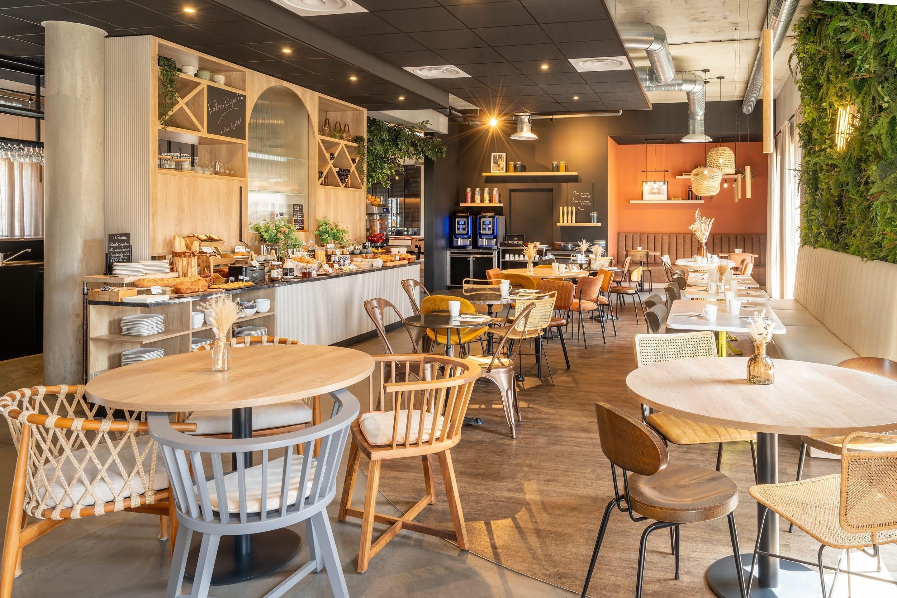 A cafe with round tables and chairs, a counter with food items, and a green wall with plants.