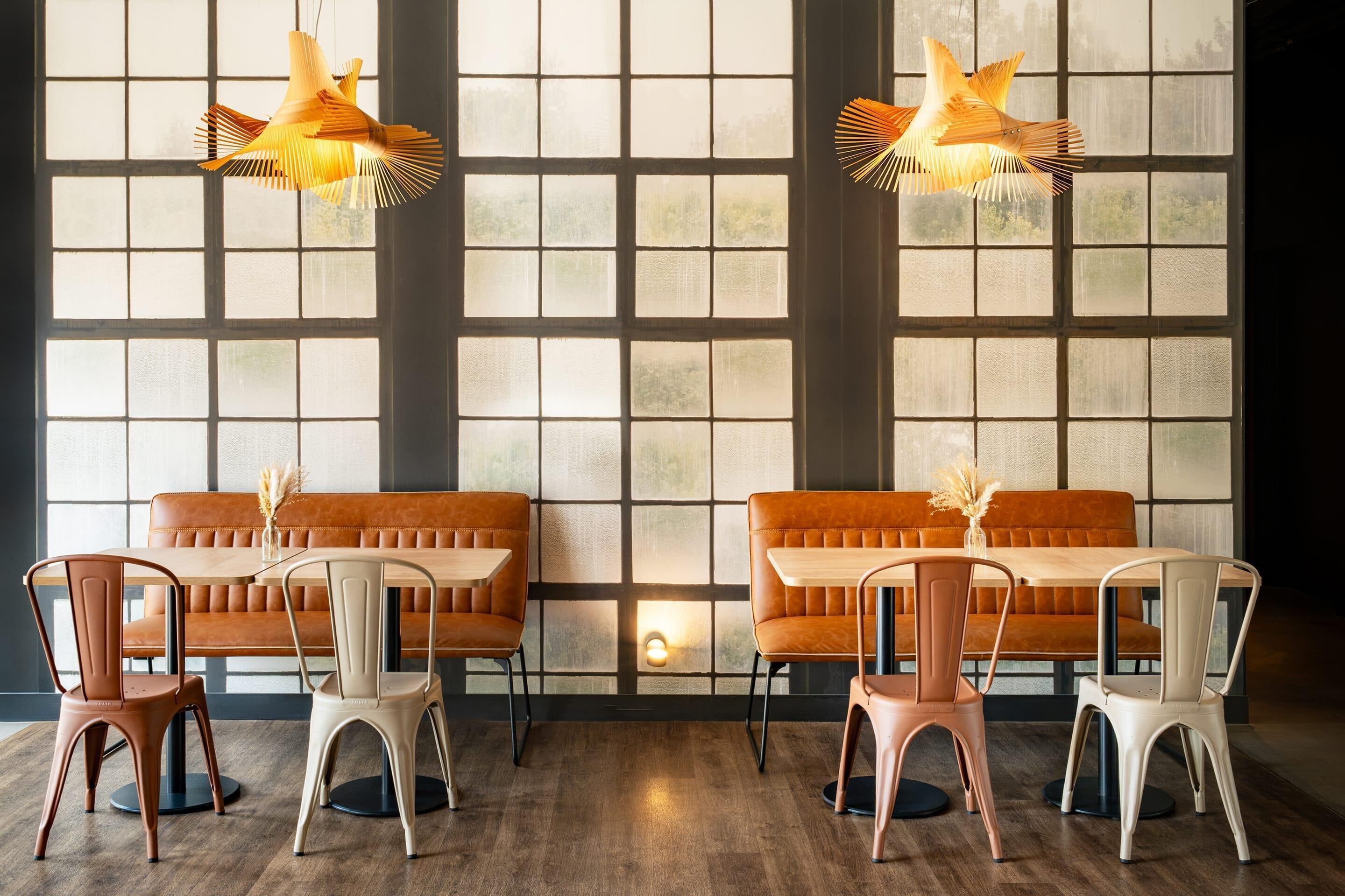 Ein Restaurant mit Holztischen und -stühlen, großen Fenstern und hängenden Pendelleuchten.