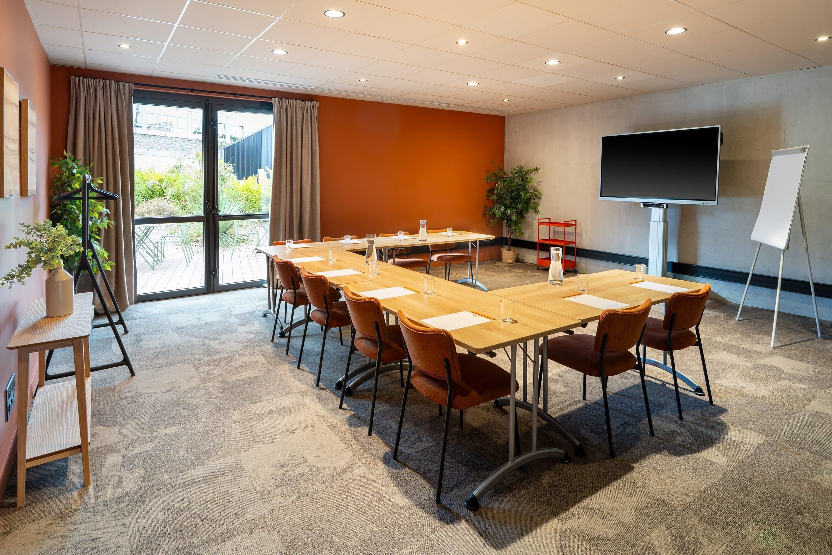 Une salle de conférence équipée d’une longue table, de chaises, d’un écran de projection et d’un tableau blanc.