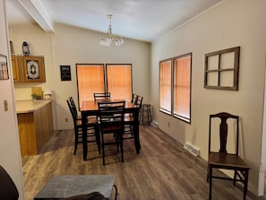 A dining area with a wooden table and chairs, a small kitchen area with a cutting board and a lantern, and a wall-mounted decorative piece.