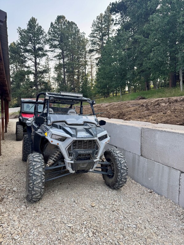 Un vehículo Polaris todoterreno estacionado sobre grava, con una barrera de concreto y árboles al fondo.