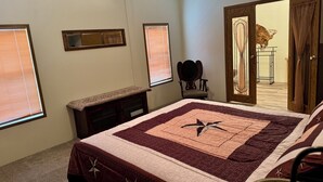 Ein Schlafzimmer mit einem großen Bett, einem Schminktisch, einem Sessel und einer Tür zu einem anderen Raum.