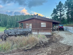 A rustic cabin with a wooden exterior, a covered porch, and a large wheelbarrow in front.