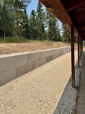 A gravel path under a wooden structure with a concrete retaining wall and trees in the background.