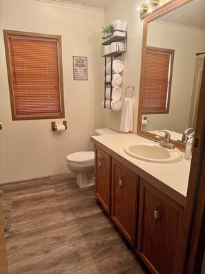 A bathroom with a toilet, sink, mirror, and towel rack. - Spud Hill Hideaway - Old West charm with modern comfort (Lead)