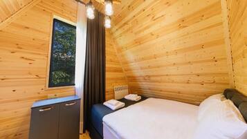 Quarto de cabana de madeira com cama, um pequeno armário, janela com cortinas e luminária no teto.