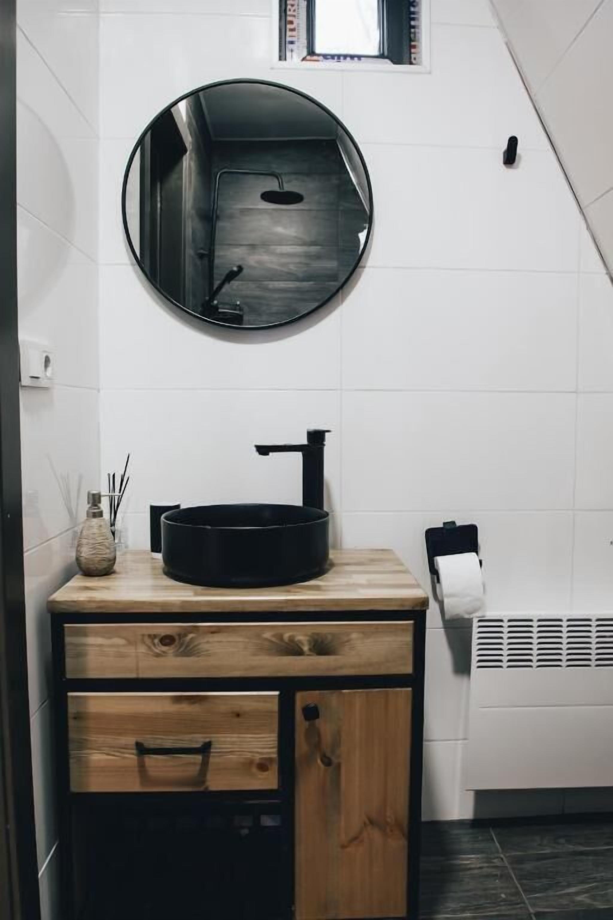 A bathroom with a round mirror, a black sink, and a wooden vanity with drawers.