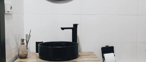A bathroom with a round mirror, a black sink, and a wooden vanity with drawers.