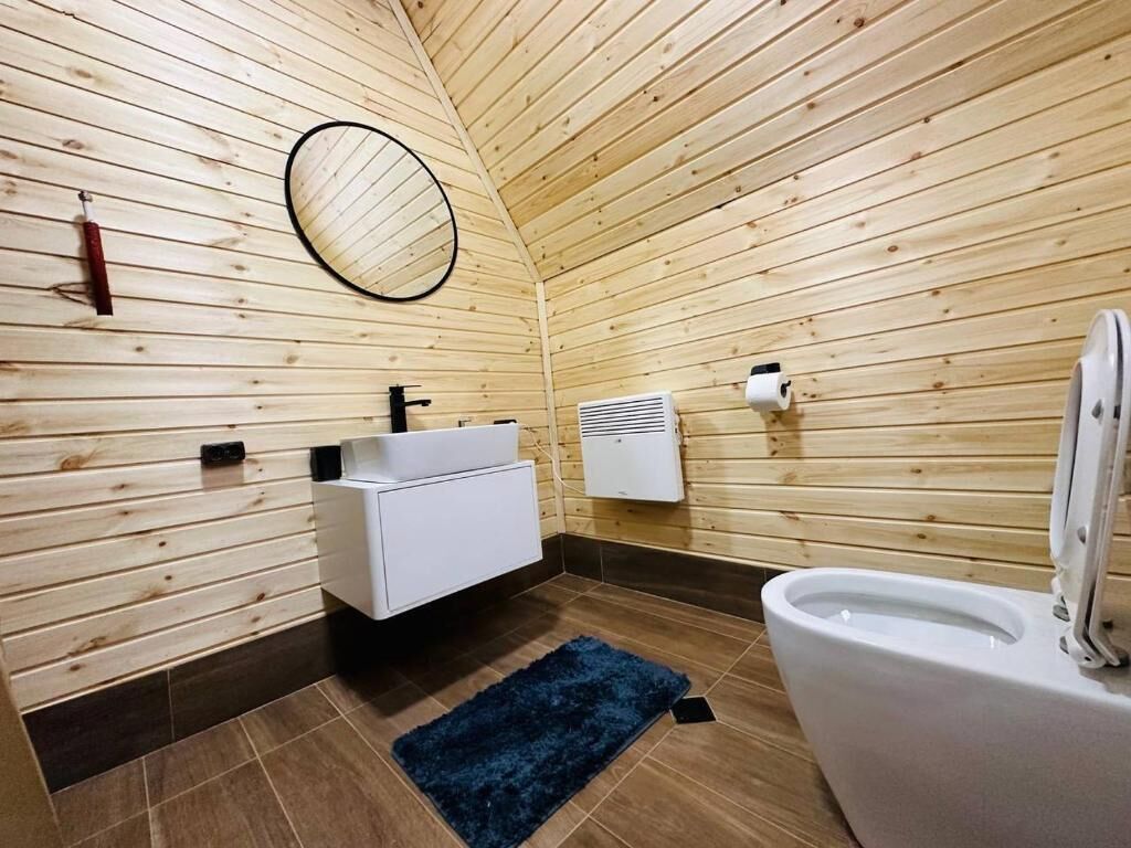 A wooden-paneled bathroom with a white sink, toilet, and a blue rug.