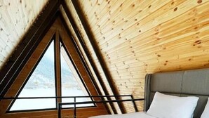 Een kamer met een schuine kap, een bed met witte lakens, een hoofdbord en een raam met uitzicht.
