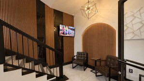 A modern interior with a staircase, wooden panel walls, a mounted TV, and a geometric light fixture.