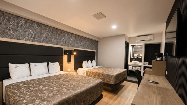 A hotel room with two beds, a desk, a mirror, and a bathroom.