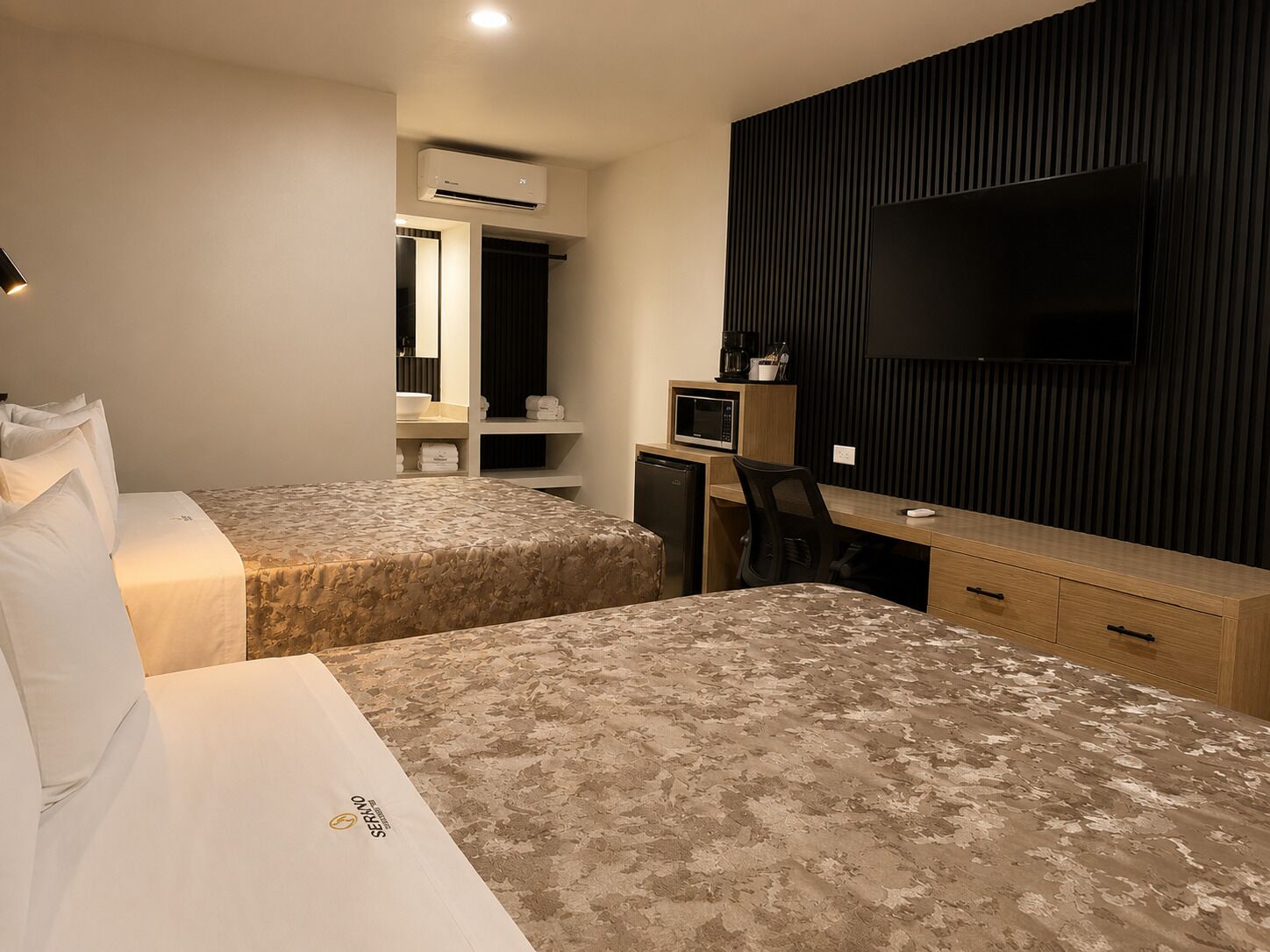 Habitación de hotel con dos camas, un escritorio, una silla, un televisor y un minibar.