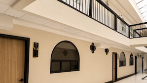 A corridor with arched windows, a wooden door, and a black railing on an upper level.